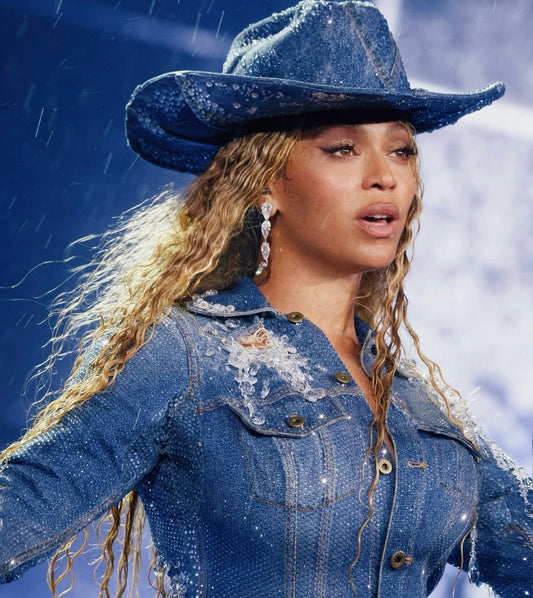 Beyoncé performing in the rain during her Cowboy Carter Tour in New Jersey 28th May 2025, wearing a denim cowboy hat and long wavy blonde hair.